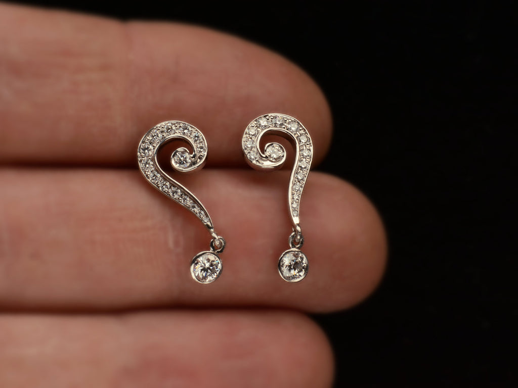 Platinum question mark-shaped earrings with diamonds on a hand against a black background