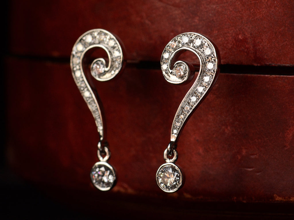Angled view of EB Question Mark Stud Earrings with brilliant cut diamonds set in platinum, shown on dark red background.
