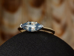 thumbnail of Angled view of EB Modern ring with marquise-shaped light blue sapphire set in a simple platinum topped yellow gold mounting, shown on black domed surface.