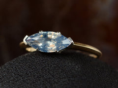 thumbnail of Angled close up view of EB Modern ring with marquise-shaped light blue sapphire set in a simple platinum topped yellow gold mounting, shown on black domed surface.