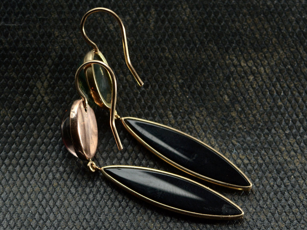Reverse sides of a pair of earrings with mismatched tops of moss agate and pink foiled rock crystal and navette shaped onyx drops, shown on dark textured background.