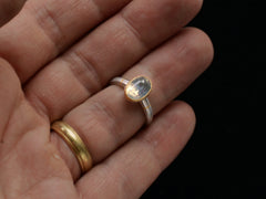 thumbnail of Minimal platinum ring with an oval pale blue opalescent sapphire set in a yellow gold collar with additional yellow gold stripes on the shank. Shown on hand.