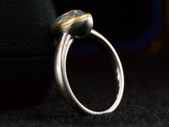 thumbnail of Angled side profile view of platinum ring with an oval pale blue opalescent sapphire set in a yellow gold collar with additional yellow gold stripes on the shank. Shown on dark background.