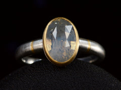 thumbnail of Front view of platinum ring with an oval pale blue opalescent sapphire set in a yellow gold collar with additional yellow gold stripes on the shank. Shown on dark background.
