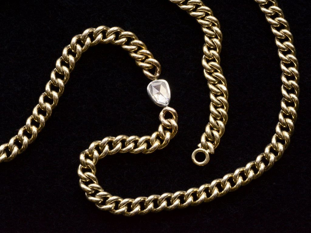 Detail of curb link yellow gold chain necklace with a platinum bezel set rose cut diamond, shown on black background.