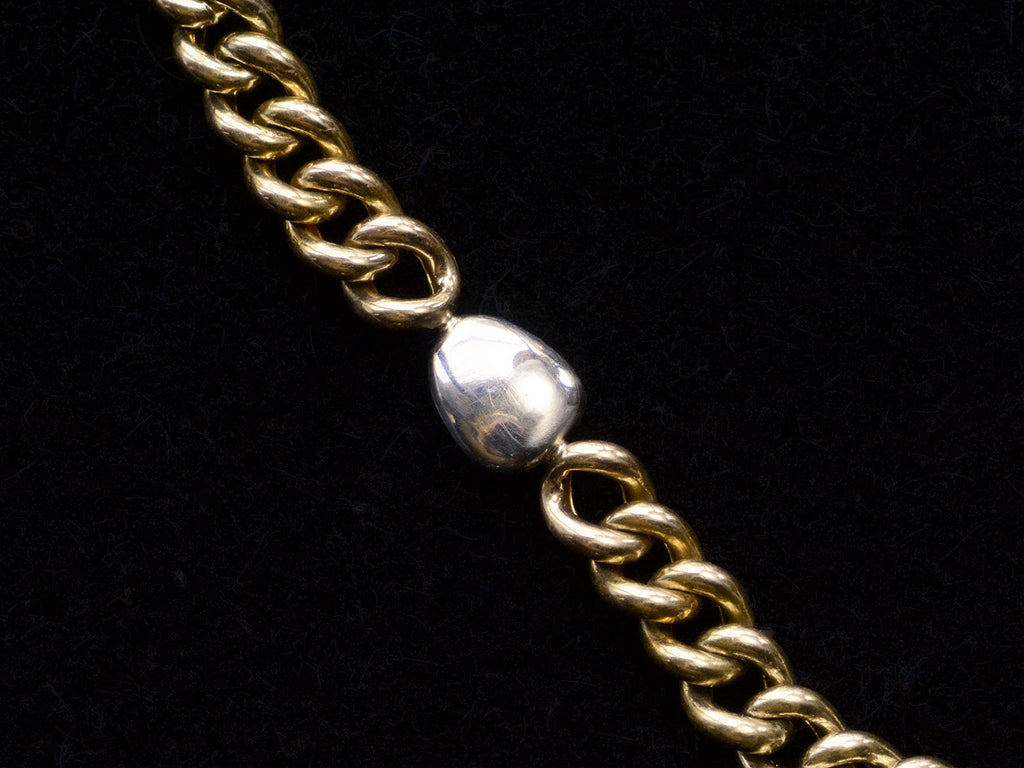 Close up of reverse side of platinum diamond setting and yellow gold curb link chain, on black background.