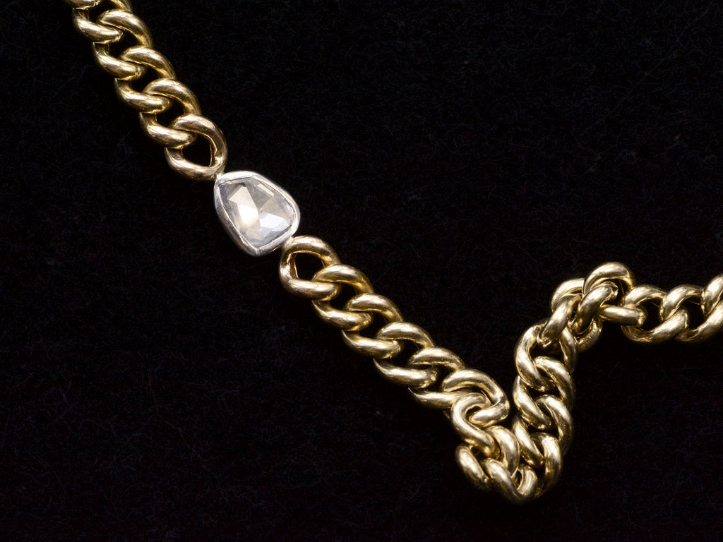 Close up of front of curb link yellow gold chain necklace with a platinum bezel set rose cut diamond, shown on black background.