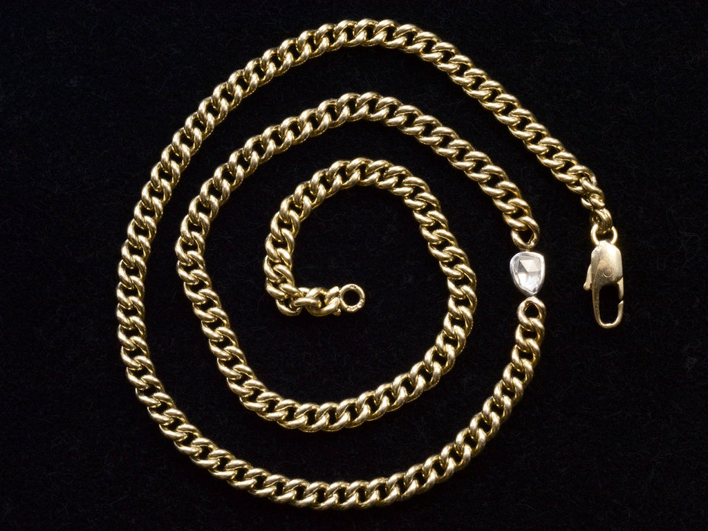 Curb link yellow gold chain necklace with a platinum bezel set rose cut diamond, shown on spiraled on black background.