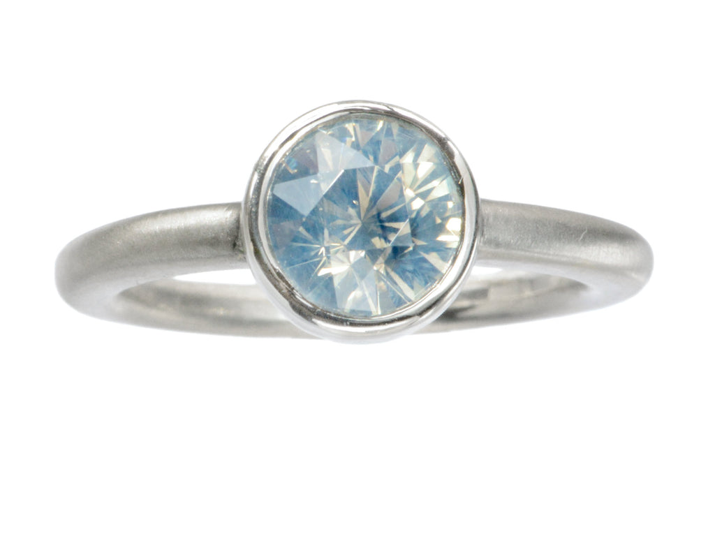 Simple round opalescent light blue sapphire in a platinum bezel with a rounded matte platinum shank, shown on white background.