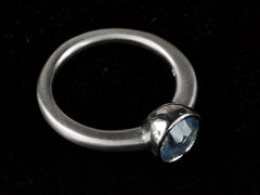 thumbnail of Elevated angled view of a round opalescent light blue sapphire in a platinum bezel with a rounded matte platinum shank, shown on black background.