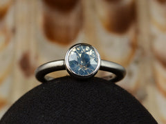 thumbnail of Front view of a round opalescent light blue sapphire in a platinum bezel with a rounded matte platinum shank, shown on domed black surface.