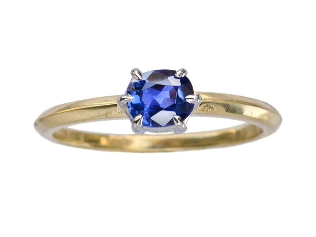 A cushion shaped blue sapphire ring set in platinum prongs over an 18K yellow gold knife edge shank, shown on white background.