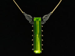 thumbnail of Detail of a pendant with a long florescent lime green uranium glass stone set in blackened silver with gold beads and wings on the mounting (on black background)