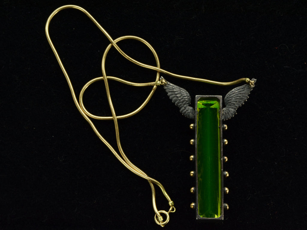 Reverse side of pendant with a long florescent lime green uranium glass stone set in blackened silver with gold beads and wings on the mounting and yellow gold snake chain (on dark background)