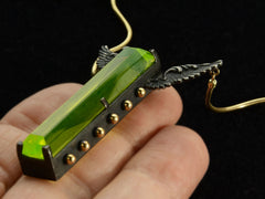 thumbnail of Angled detail of a pendant with a long florescent lime green uranium glass stone set in blackened silver with gold beads and wings on the mounting and yellow gold snake chain (on hand)