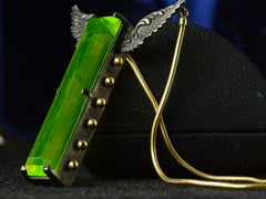 thumbnail of Angled view of pendant with a long florescent lime green uranium glass stone set in blackened silver with gold beads and wings on the mounting and yellow gold snake chain (on dark background)