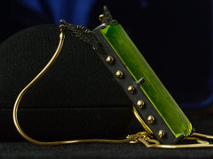 thumbnail of Left side of pendant with a long florescent lime green uranium glass stone set in blackened silver with gold beads and wings on the mounting and yellow gold snake chain (on dark background)