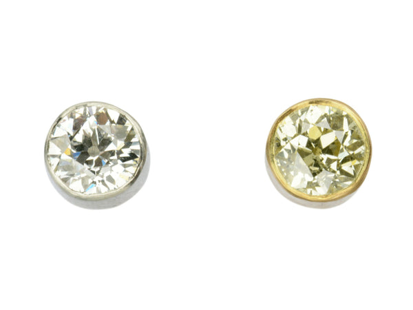 Pair of EB Modern old European cut diamond studs, mismatched with a white diamond in platinum and a yellow diamond in 22K yellow gold. Shown on white background.