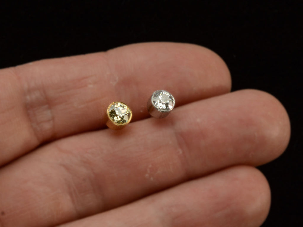 Pair of EB Modern old European cut diamond studs, mismatched with a white diamond in platinum and a yellow diamond in 22K yellow gold. Shown on hand for scale.