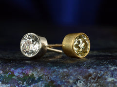 thumbnail of Angled views of pair of EB Modern old European cut diamond studs, mismatched with a white diamond in platinum and a yellow diamond in 22K yellow gold. Shown on dark colorful background.