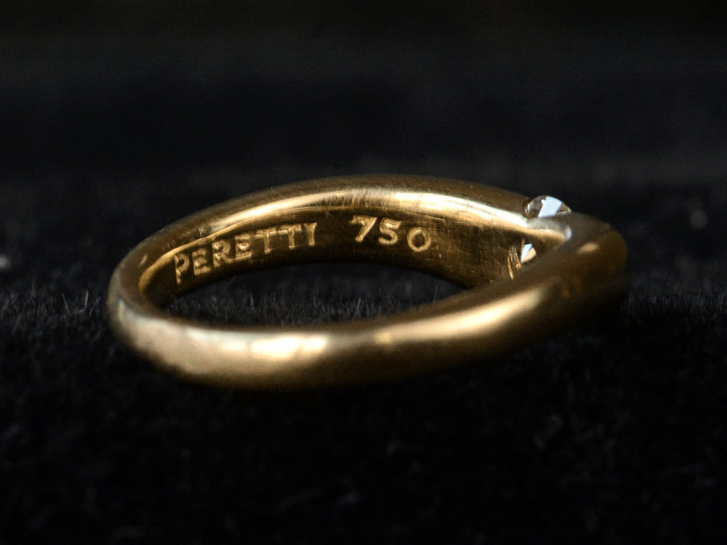 Detail view of the inside of vintage gold ring stamped with "PERETTI 750" shown on dark background.