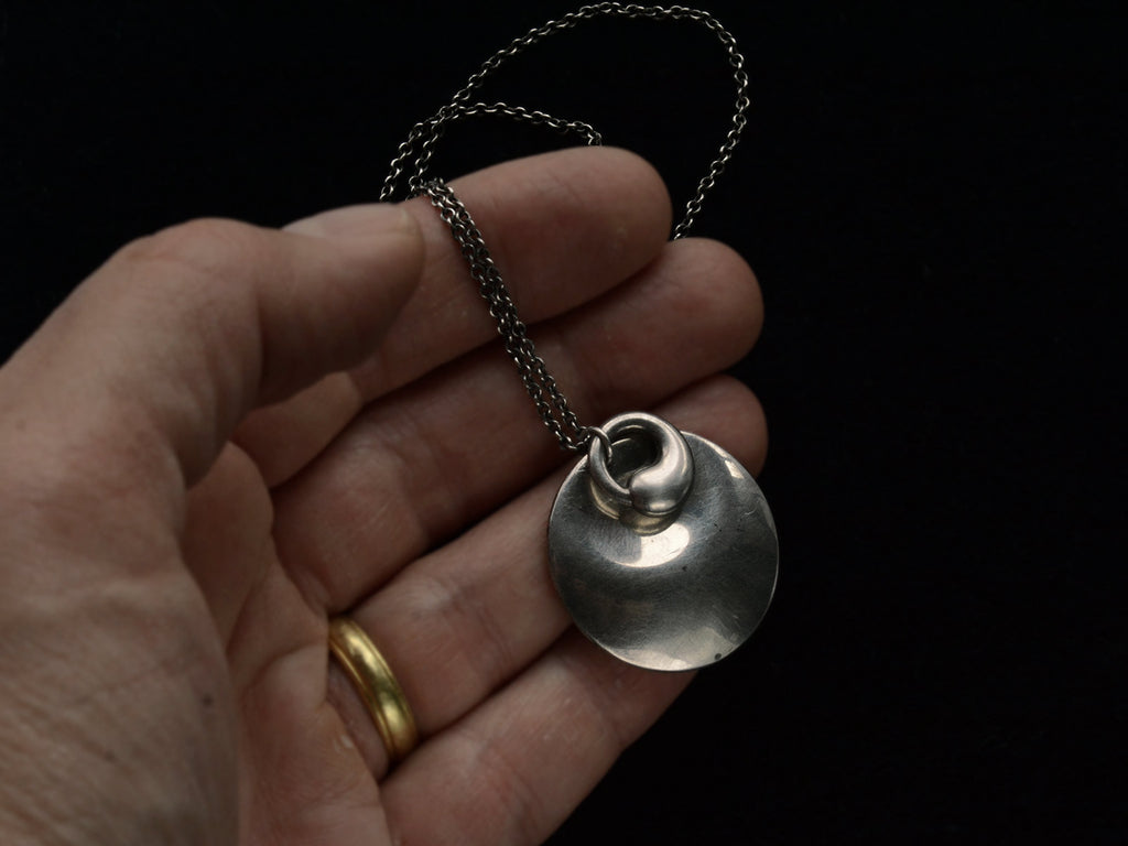 Pair of organic and minimal silver Elsa Peretti overlapping pendants hung on chain, held in hand.