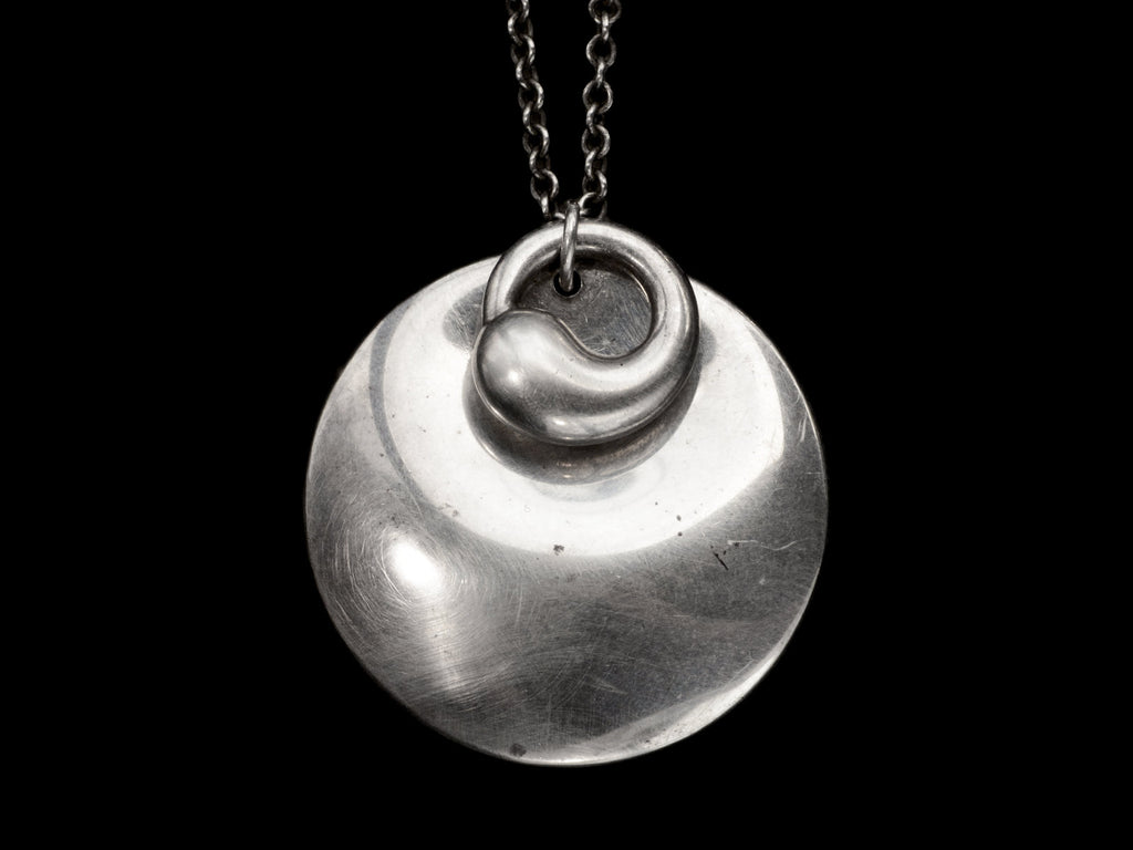 Pair of overlapping organic and minimal silver Elsa Peretti pendants, on black background. 