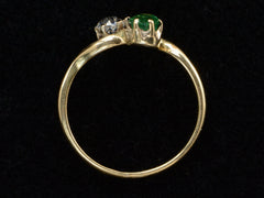 thumbnail of Side profile of an antique Art Nouveau yellow gold wave-form ring with an emerald set opposite an old mine cut white diamond, shown on black background.