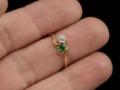 thumbnail of An antique Art Nouveau yellow gold wave-form ring with an emerald set opposite an old mine cut white diamond, shown on finger.