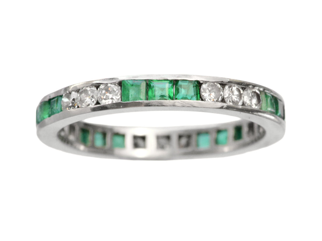 Vintage platinum eternity ring with alternating emeralds and diamonds on a white background

