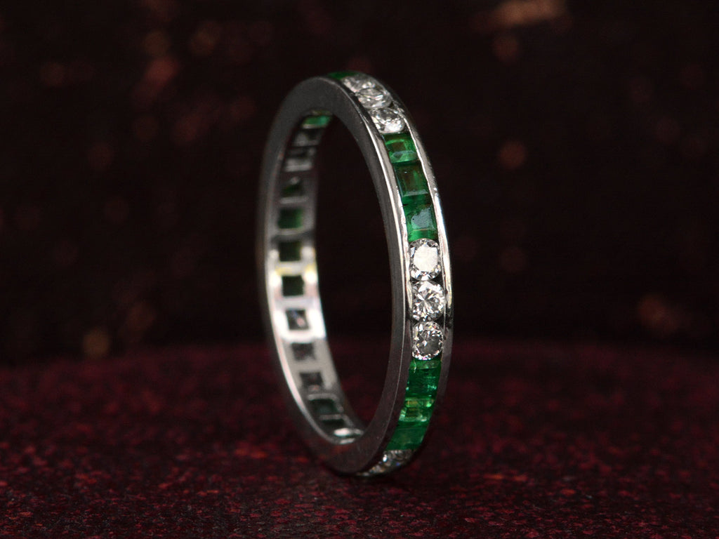 Vintage platinum eternity ring with alternating emeralds and diamonds on a dark background