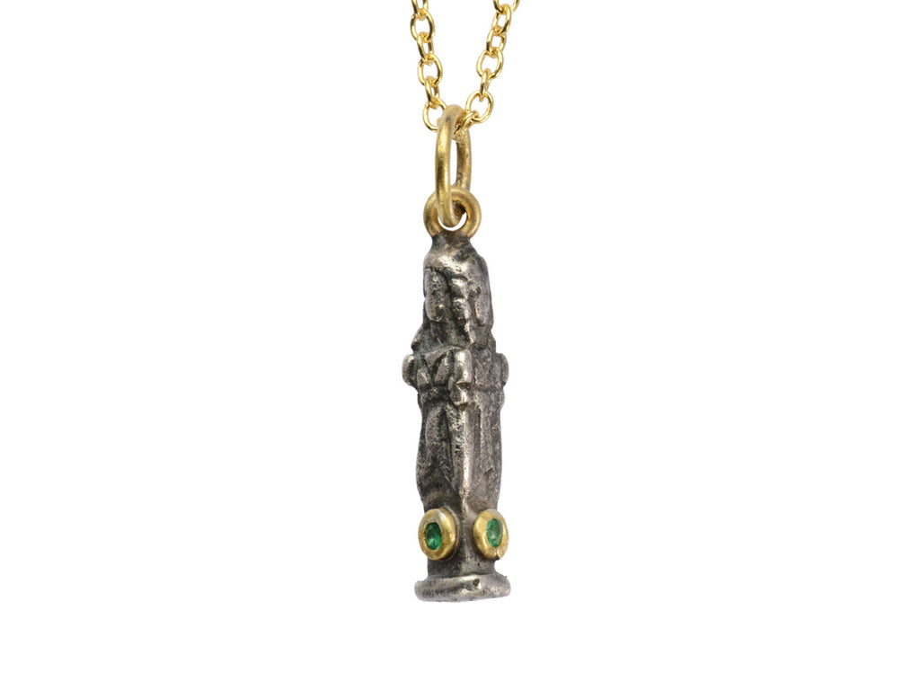 A small three sided figural pendant in silver and 22K yellow gold with emeralds, shown on white background.