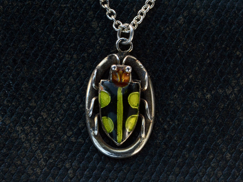 Detail of c1920 Deco silver pendant with an red-headed, black and green enamel beetle set on an oval frame, shown on dark textured background