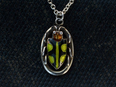 thumbnail of Detail of c1920 Deco silver pendant with an red-headed, black and green enamel beetle set on an oval frame, shown on dark textured background