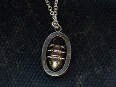 thumbnail of Reverse side of c1920 Deco silver pendant with a beetle set in an oval frame, shown on dark textured background. A "SILVER" stamp is visible.