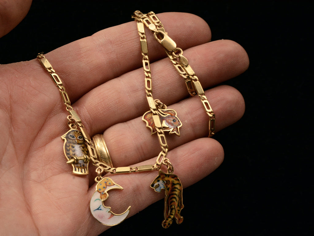 c1970 Enamel Charms Necklace (an owl, a moon, a tiger and a goldfish) in yellow gold. On a hand for scale.