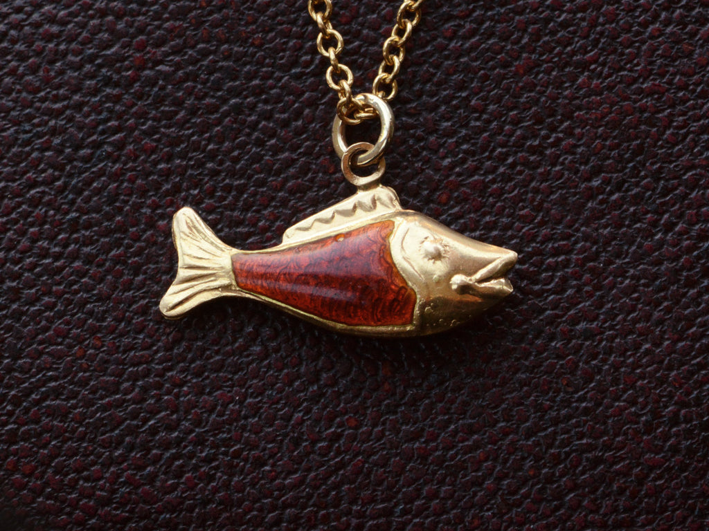 Vintage fish charm, facing right, in yellow gold and orange enamel, shown on dark textured background.