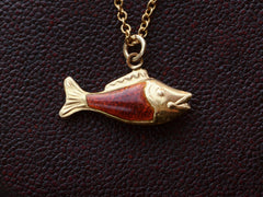 thumbnail of Vintage fish charm, facing right, in yellow gold and orange enamel, shown on dark textured background.