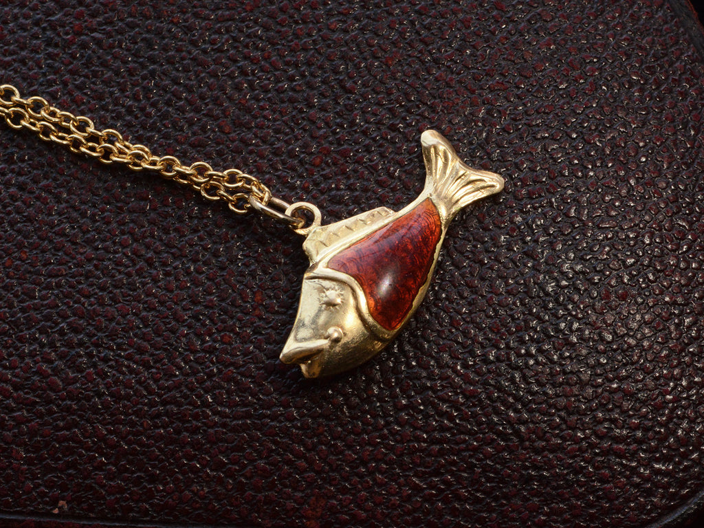 Vintage fish charm, facing left, in yellow gold and orange enamel, shown on dark textured background.