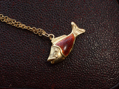 thumbnail of Vintage fish charm, facing left, in yellow gold and orange enamel, shown on dark textured background.