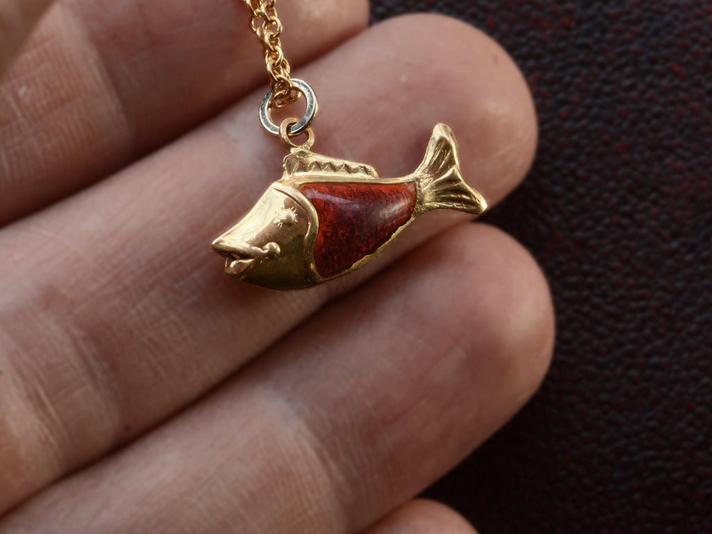 Vintage fish charm, facing left, in yellow gold and orange enamel, shown on hand.