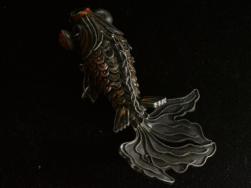 Top view of vintage c1950 Chinese articulated fish pendant with orange enamel and filigree, shown on dark background.