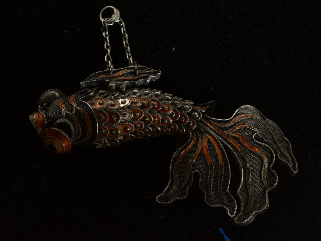 A vintage c1950 Chinese articulated fish pendant with orange enamel and filigree, shown on dark background.
