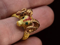 thumbnail of Detail view of a c1960 vintage ram's head ring in yellow gold with green emerald eyes and yellow and orange enamel details. Shown on finger.