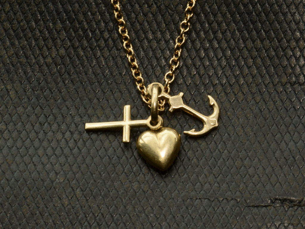 Vintage gold necklace with heart, anchor, and cross pendant on a textured dark background