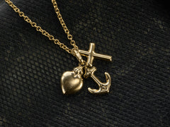 thumbnail of Detail of Italian yellow gold charm necklace with a cross, a heart and an anchor hanging on cable chain, shown on dark textured background.