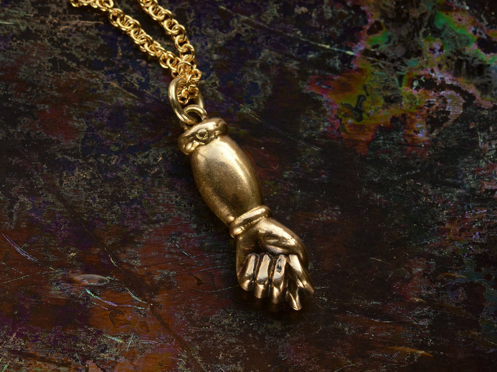 Vintage gold hand-shaped figa pendant on a chain against a dark background