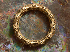 thumbnail of Side profile of rosy-yellow gold eternity band with geometric filigree. Shown on colorful background.