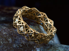 thumbnail of Angled front view of rosy-yellow gold eternity band with geometric filigree and brown diamonds. Shown on dark background.