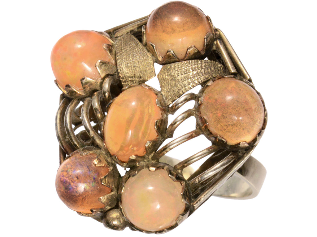 Right angled view of pentagonal Arts & Crafts movement ring with six fire opal cabochons set in a filigreed mounting, shown on white background.